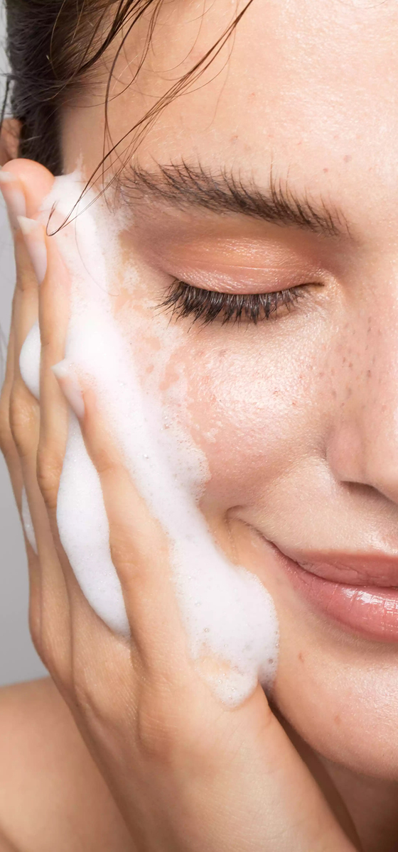 immagine ragazza che sorride, con due mani con mousse per pulirsi il viso. Si tocca le guance